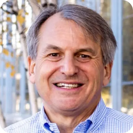 Smiling man with gray hair to the side and light blue checkered shirt