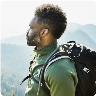 Photo of man in green shirt with black backpack and mountains behind him